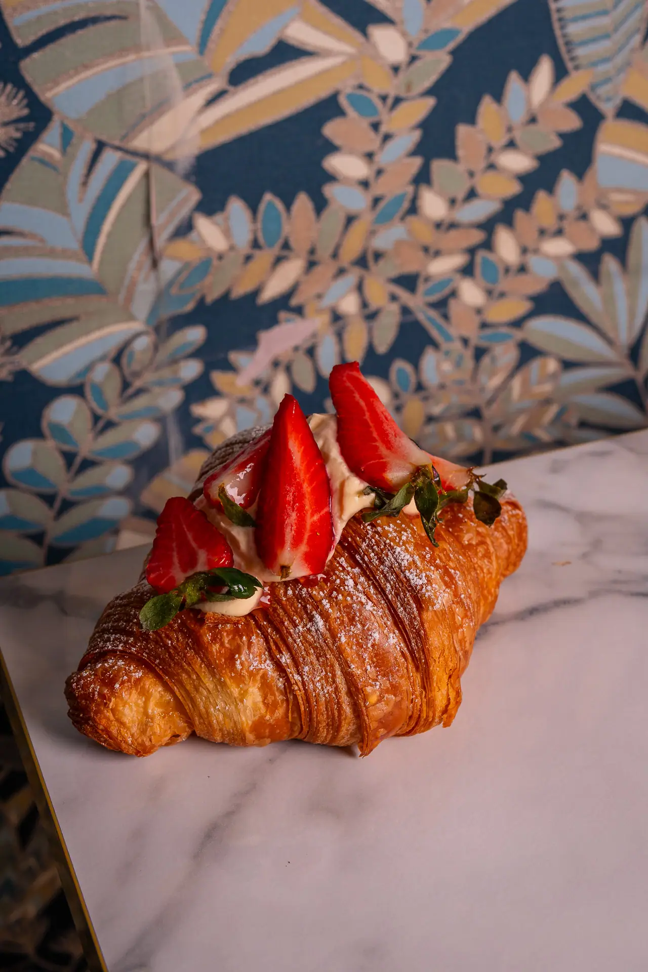 Cornetto con fragole e crema sul marmo, carta da parati blu a foglie