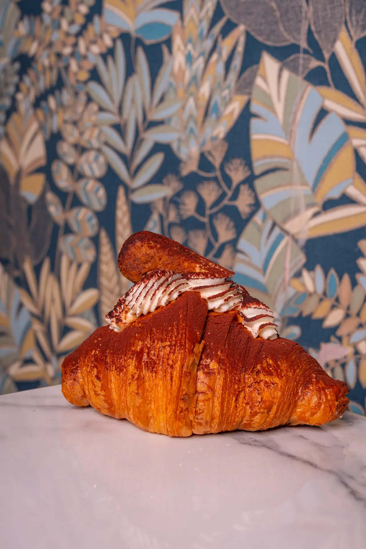 Cornetto con crema sul piano di marmo, dietro la carta da parati a foglie