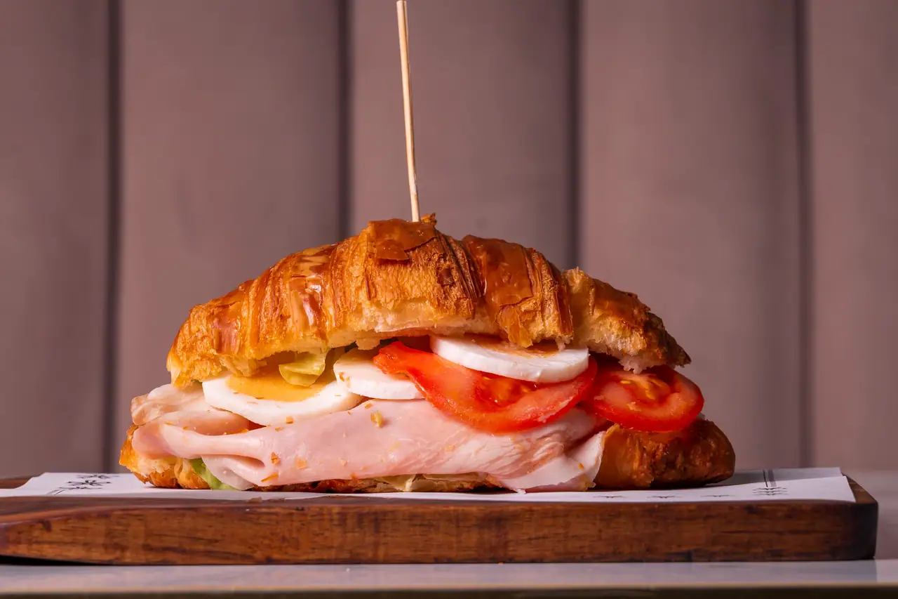 Croissant salato con uova, pomodoro e prosciutto cotto sul tagliere